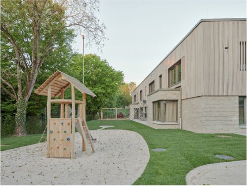 Bild der Kita Zaunkönige von außen mit Spielplatz, Rasen und blauem Himmel im Hintergrund